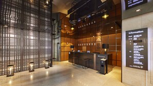 Rebedor modern d'un hotel, amb una recepció, zona de seients i un panell d'informació gran.