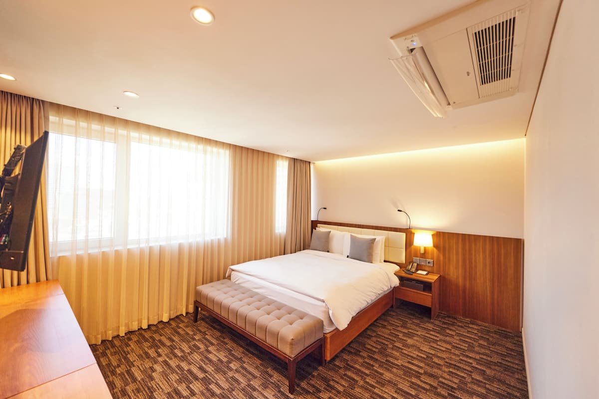 Habitación de hotel con una cama grande, un escritorio, una silla, un televisor y una ventana con cortinas.