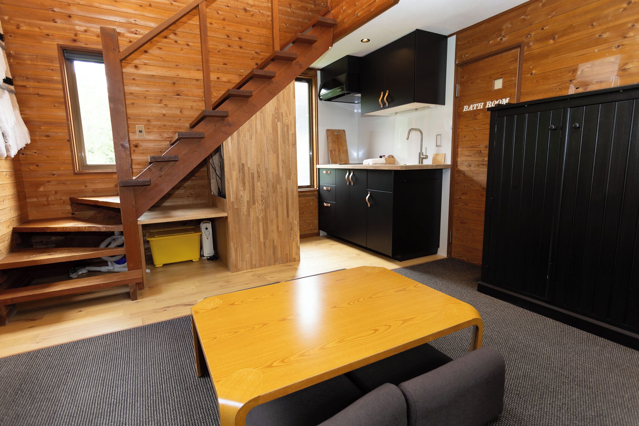 A wooden interior with a staircase, a kitchen area, and a bathroom.