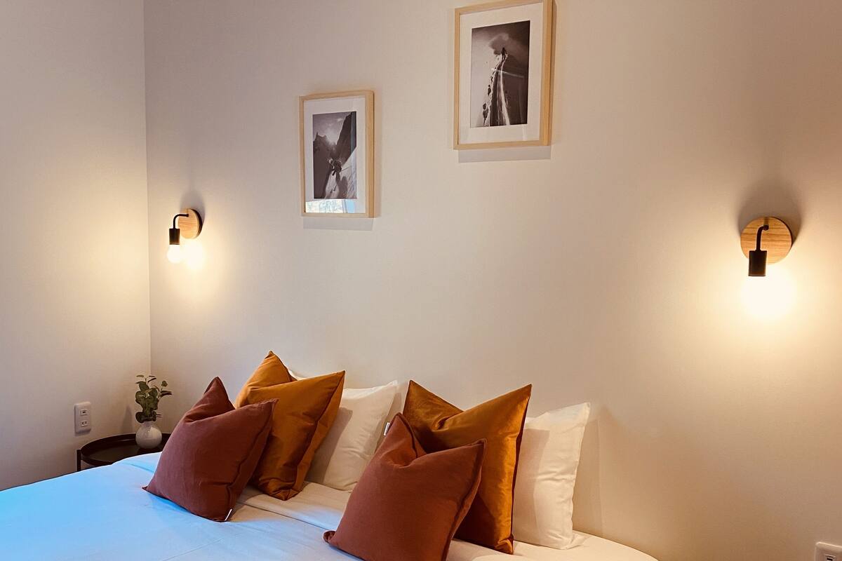 A modern bedroom with a large bed, two wall-mounted lights, and two framed pictures.