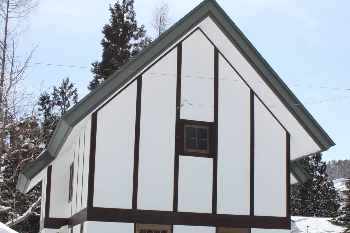 A two-story building with a steep gable roof, a central chimney, and a snow-covered ground.