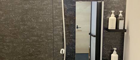 A modern bathroom with a black marble wall, a handheld showerhead, a built-in toilet, a mirror, and two bottles of lotion on a shelf.