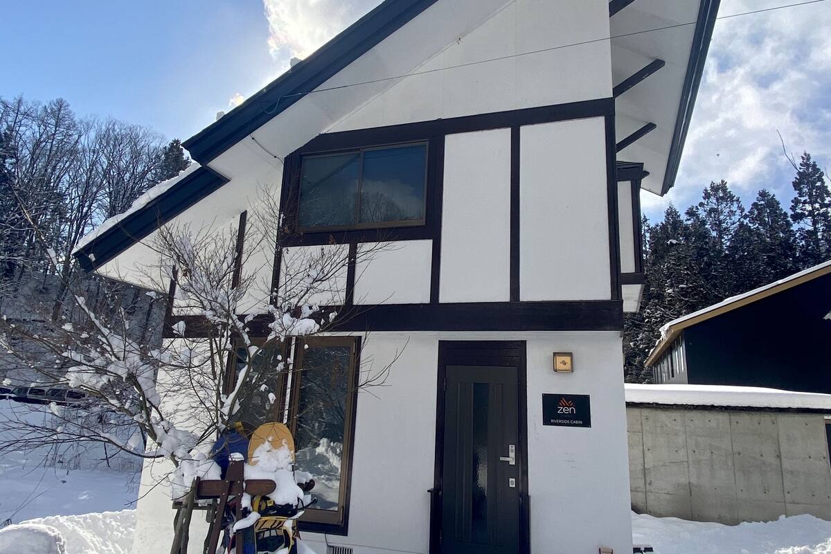 A modern two-story cabin with a snow-covered entrance and a visible sign indicating it is a Zen resort.