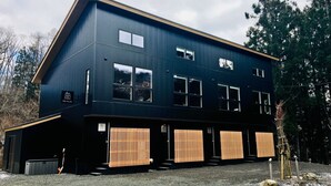 Un edificio moderno de dos pisos con fachada oscura, múltiples ventanas y un garaje con contraventanas de madera.