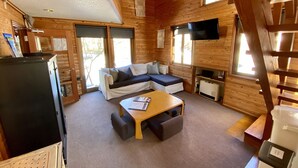 Un interior de cabaña acogedor con un sofá, una mesa pequeña, un televisor y un refrigerador.
