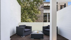 A balcony with two dark wicker sofas and a central coffee table, surrounded by white walls and a wooden deck. - Sydney Boutique Hotel (Darlinghurst)