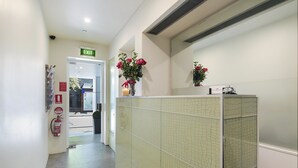 A hallway with a green tiled wall, an exit sign, a fire extinguisher, and a vase with flowers. - Sydney Boutique Hotel (Darlinghurst)