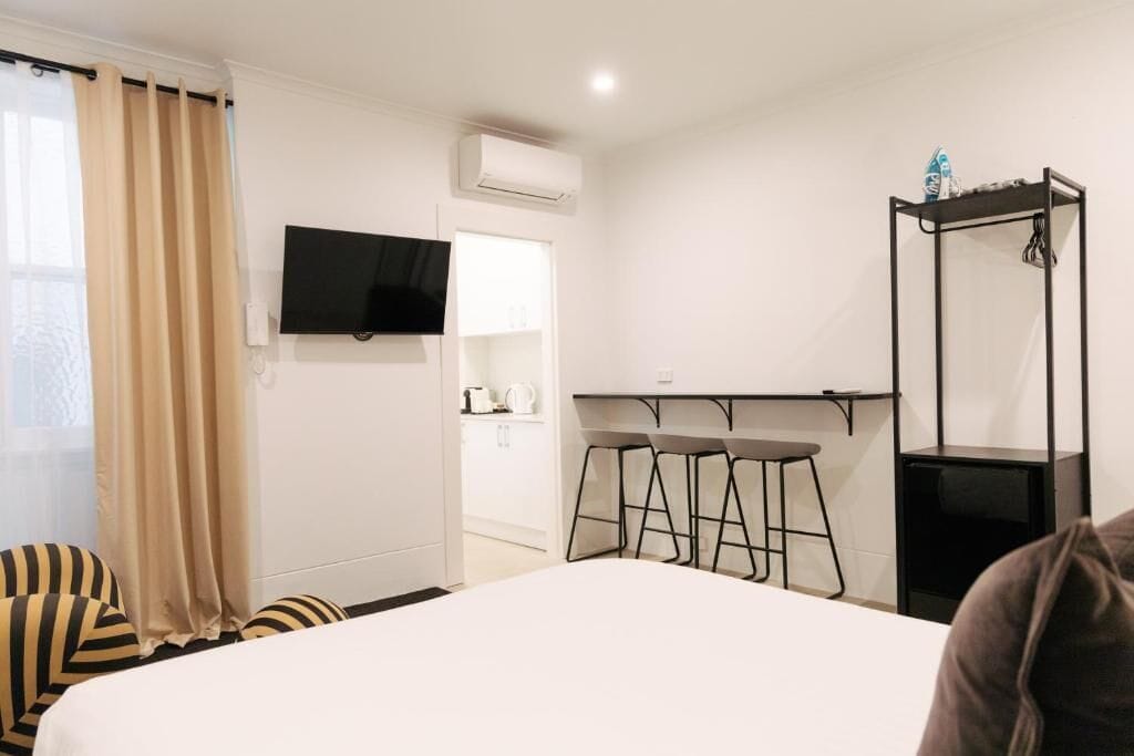 Een hotelkamer met een bed, een aan de muur bevestigde televisie, een klein keukenhoekje en een zithoek met krukken.
