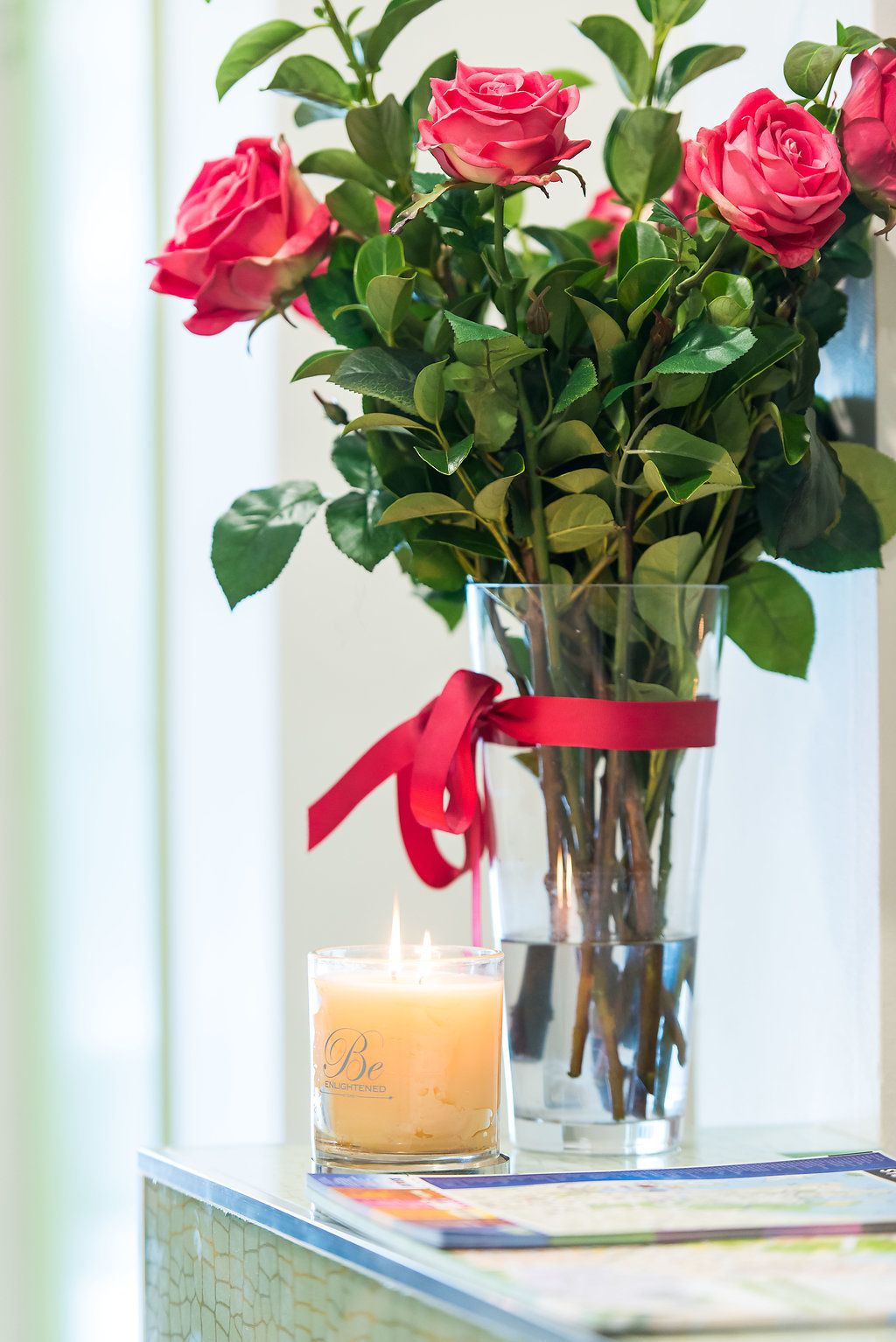 Un vase rempli de roses roses et une bougie posés sur une table.