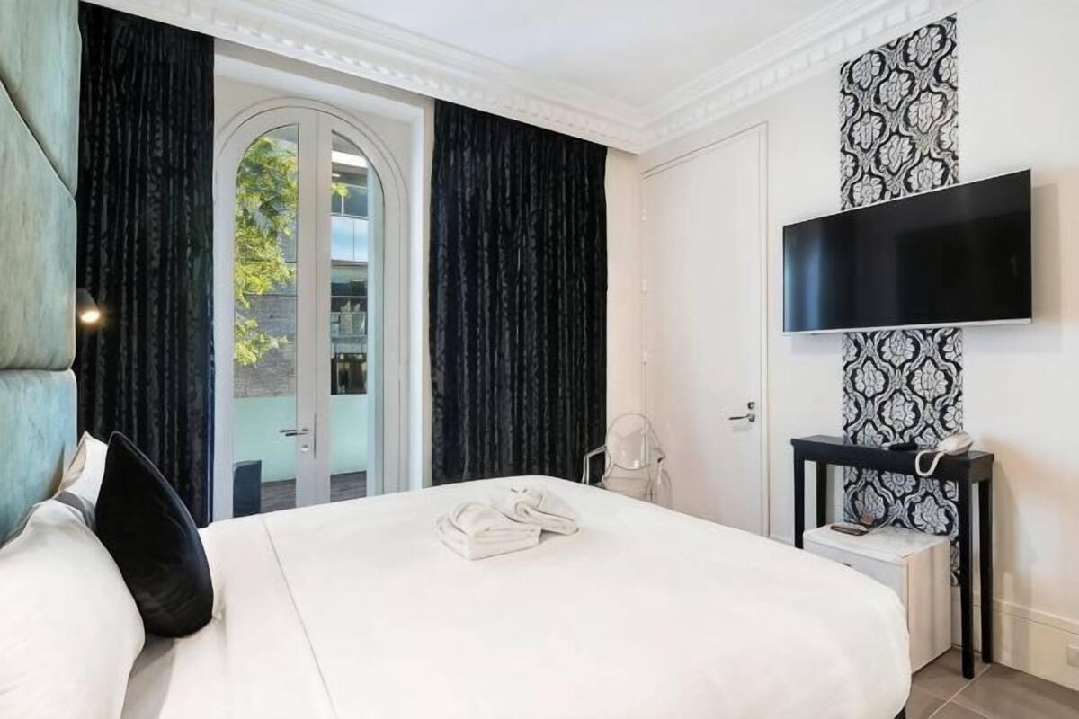 Habitación de hotel con cama, televisor, escritorio y puerta que da a un balcón.