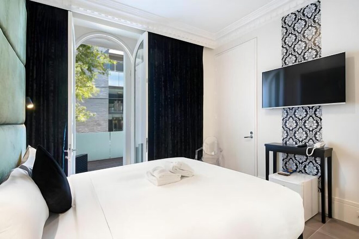 Habitación de hotel con una cama grande, un televisor de pantalla plana, una mesita de noche y vistas al exterior.
