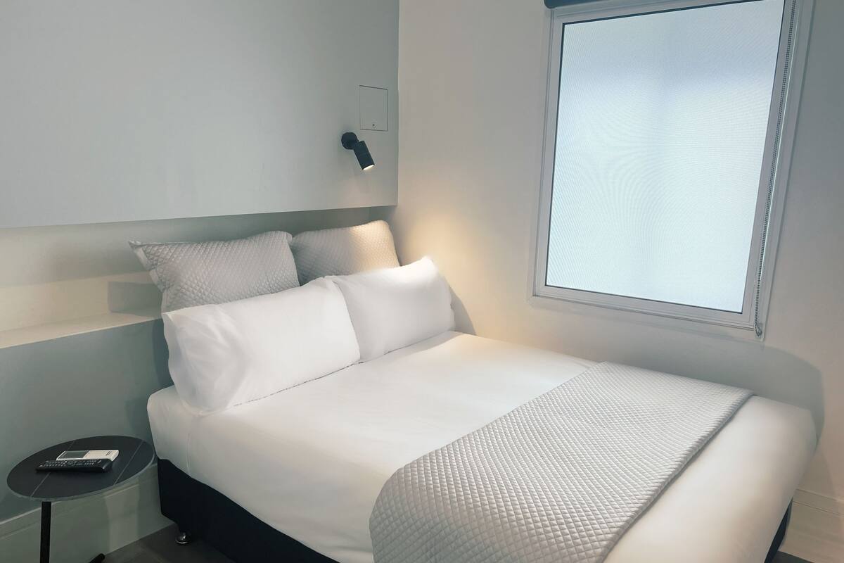 Un dormitorio moderno con una cama grande, una mesita de noche con lámpara y una ventana con persianas.