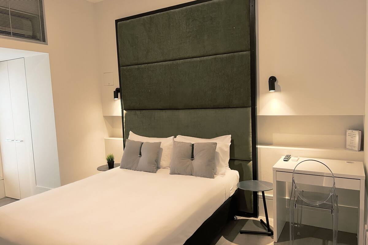 Un dormitorio moderno con una cama grande, una mesita de noche, una silla y una lámpara de pared.