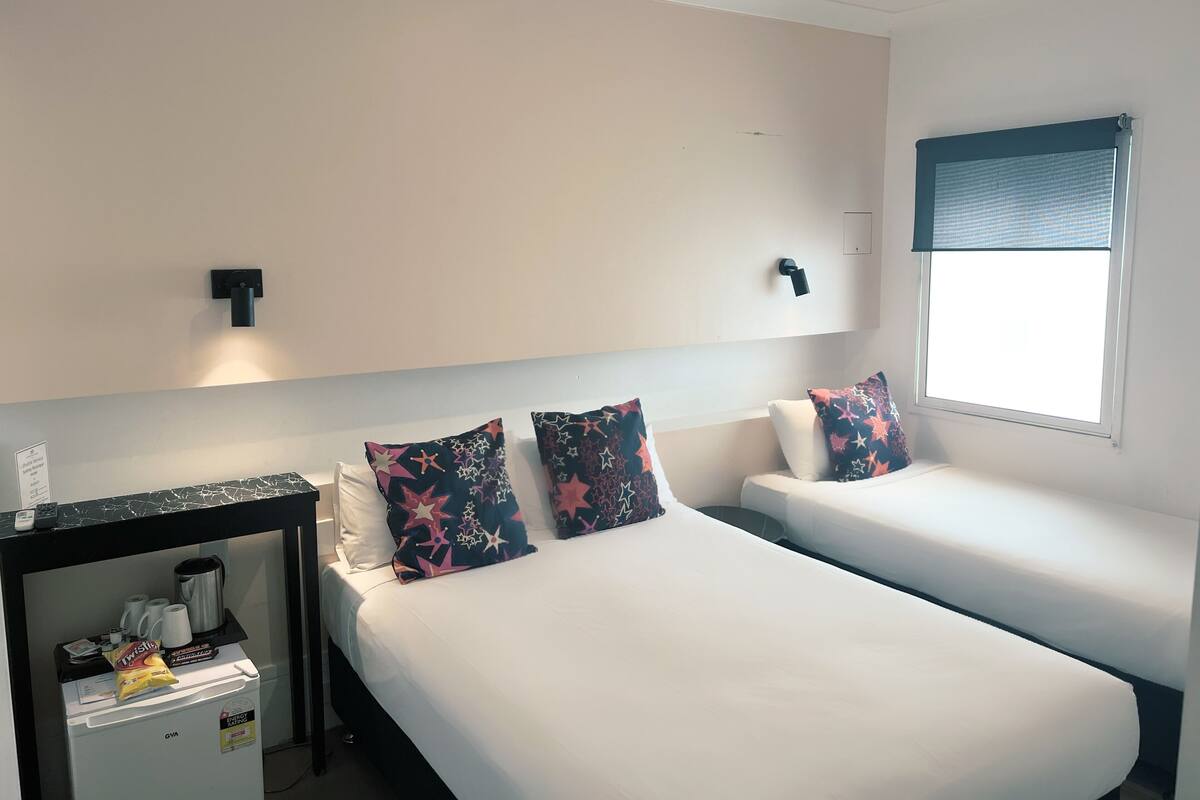 Una habitación de hotel con dos camas individuales, una mesita con cafetera y una ventana con persianas.