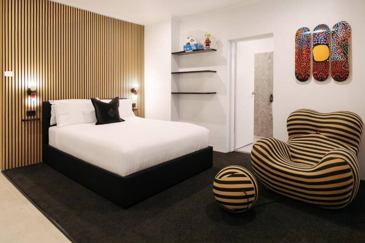 Un dormitorio moderno con una cama grande, una silla original con rayas y una pared decorada con arte.