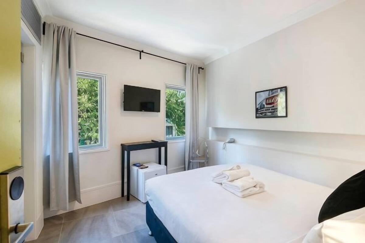 Una habitación de hotel con cama, escritorio, televisor y ventana con cortinas.