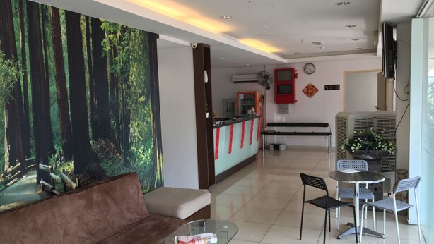 A hotel lobby with a reception desk, a brown sofa, a glass coffee table, and a seating area with chairs and a small table.