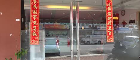 A storefront with glass doors, red banners, and a potted plant outside.