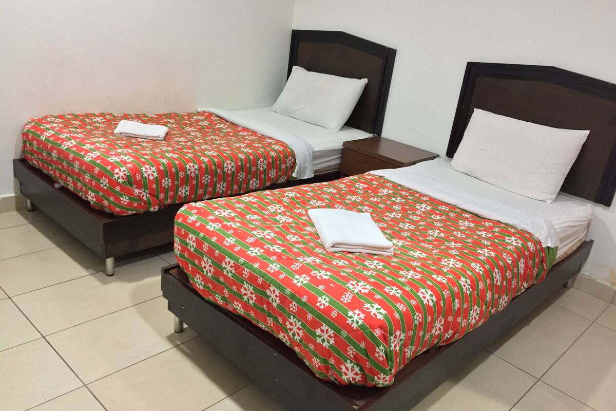 Two single beds with red and white bedding, a wooden headboard, and a small bedside table with a white pillow.