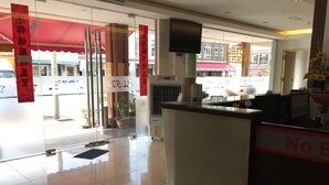 A hotel reception area with a glass door entrance, a reception desk, and a TV mounted on the wall.