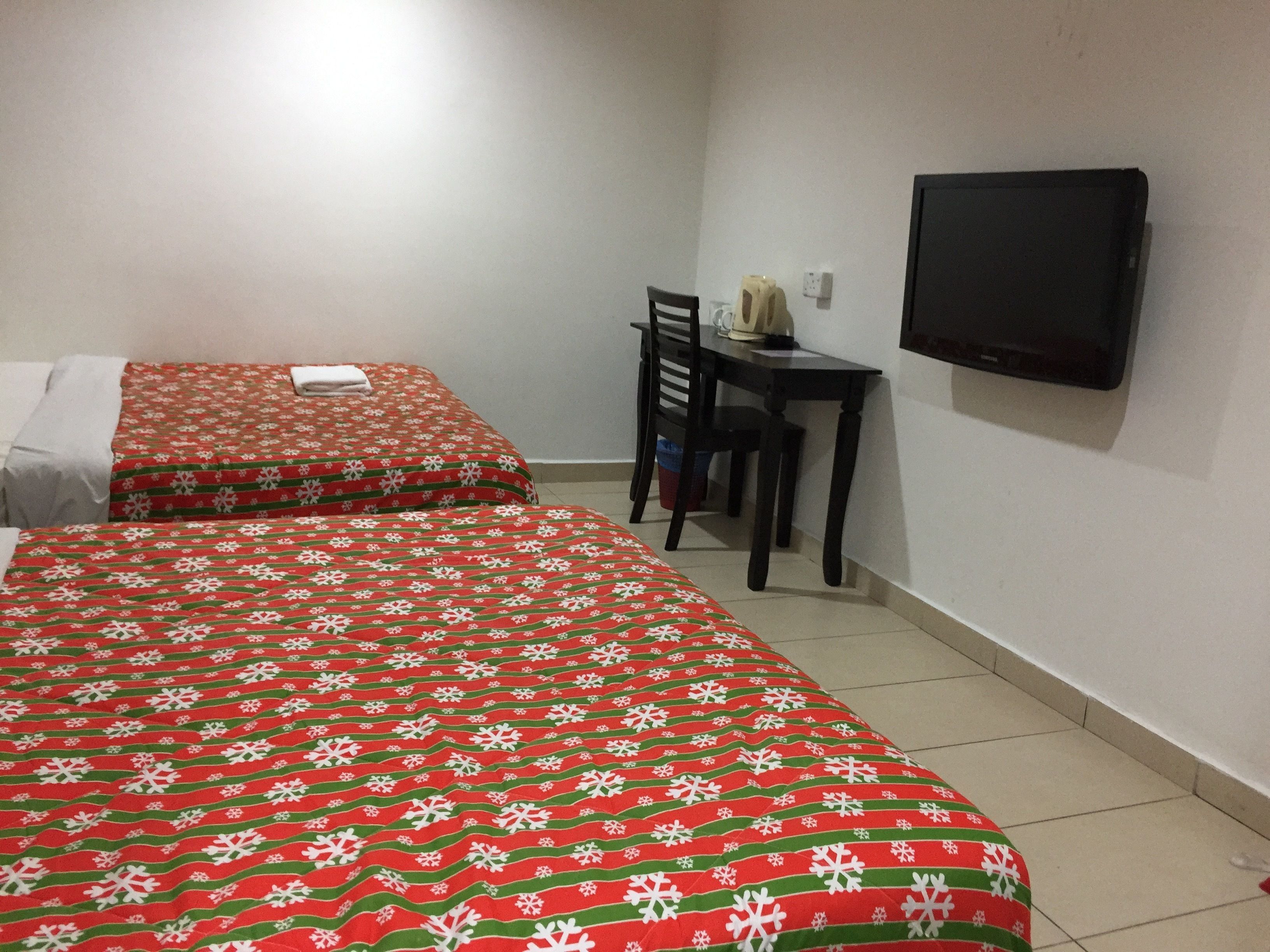 Dos camas con ropa de cama roja y verde, un escritorio con una silla y un televisor en la pared.