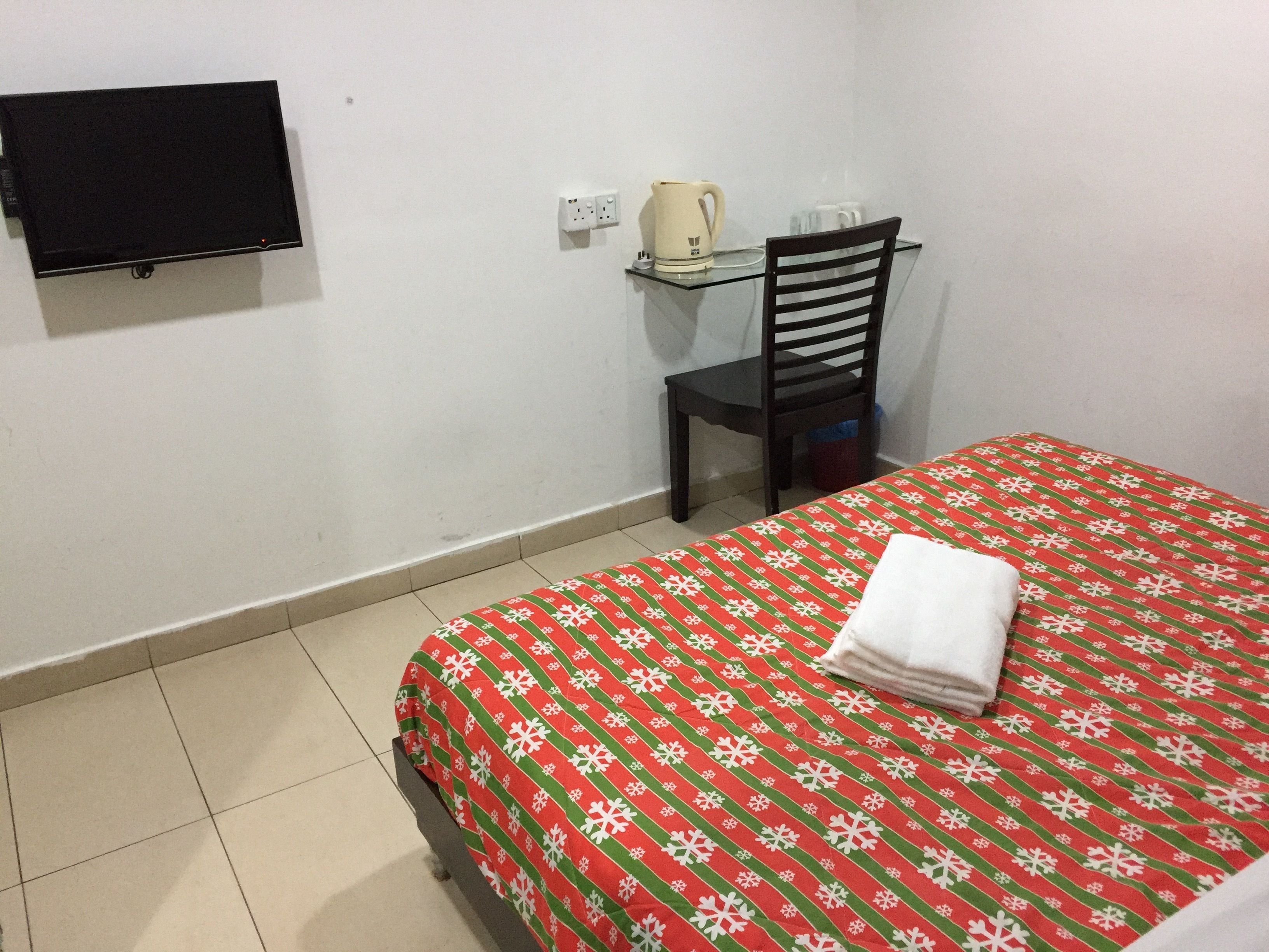 Una habitación de hotel con una cama, una silla, un televisor montado en la pared y una cafetera sobre la mesa.