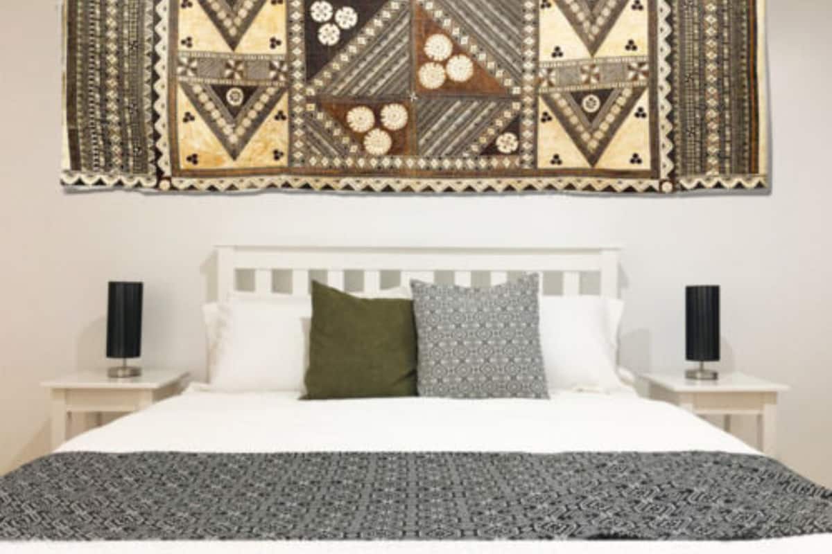A bedroom with a bed, white headboard, two bedside tables with lamps, and a patterned tapestry on the wall.
