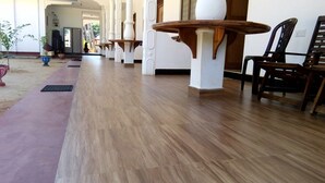 Un pasillo con suelo de madera, pilares blancos y mesas y sillas de madera.