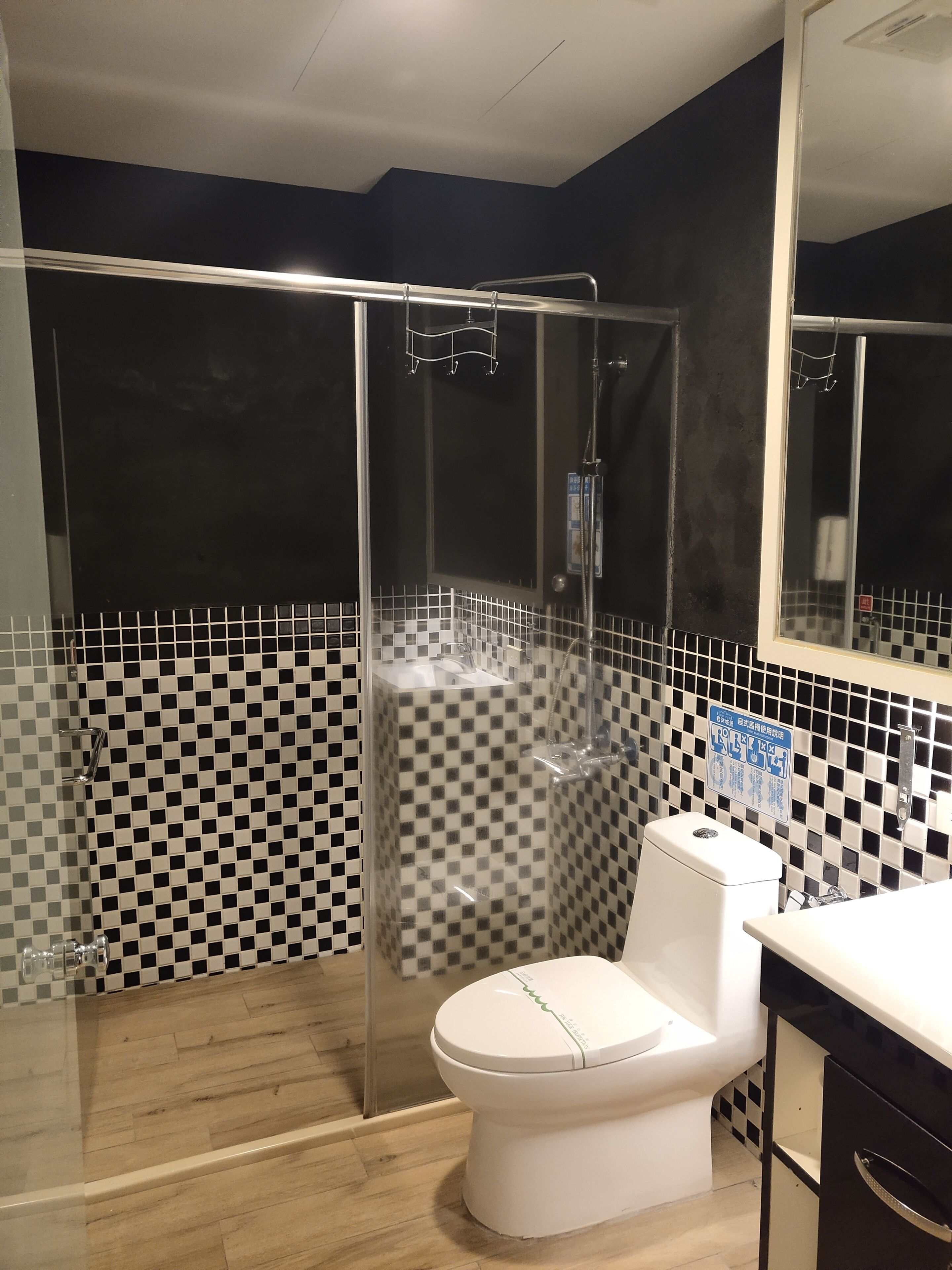 Een moderne badkamer met een douchecabine van glas, een wit toilet en een betegelde spatwand met ruitmotief.