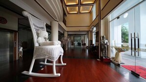 A spacious lobby with a wooden floor, a white rocking chair, and a statue. - Empire Pacific Castle (Taoyuan City)