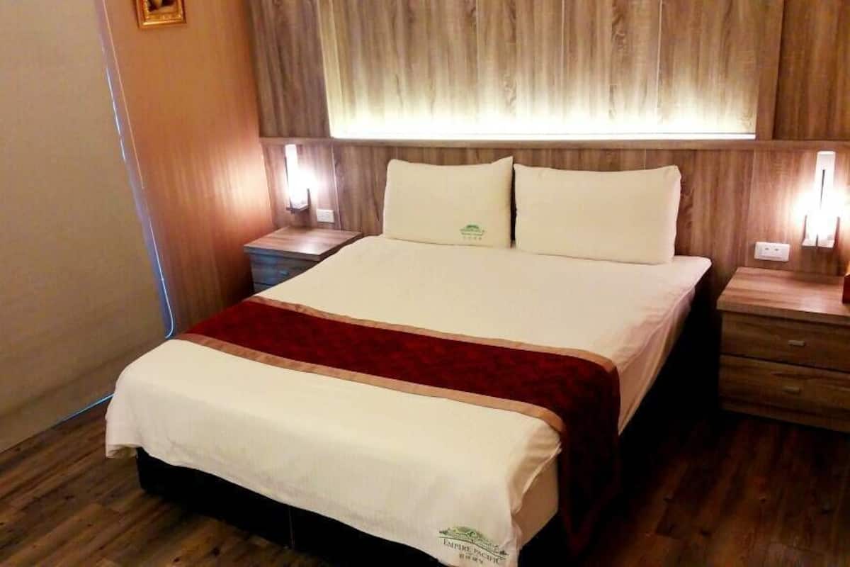 Een hotelkamer met een groot bed, houten vloeren, een nachtkastje en een bijzettafeltje.