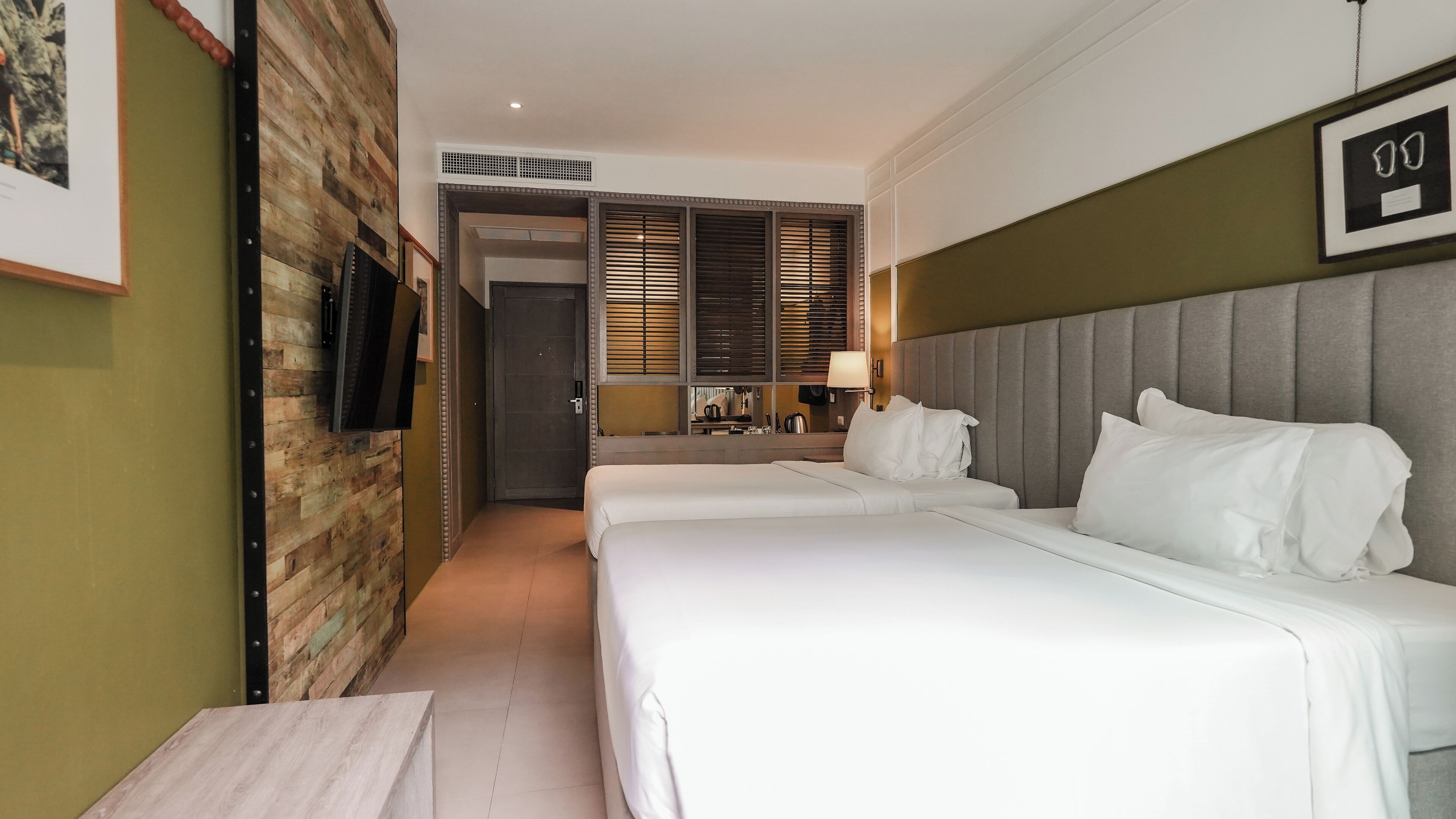 A hotel room with two beds, a television mounted on the wall, a wooden accent wall, and a framed picture.