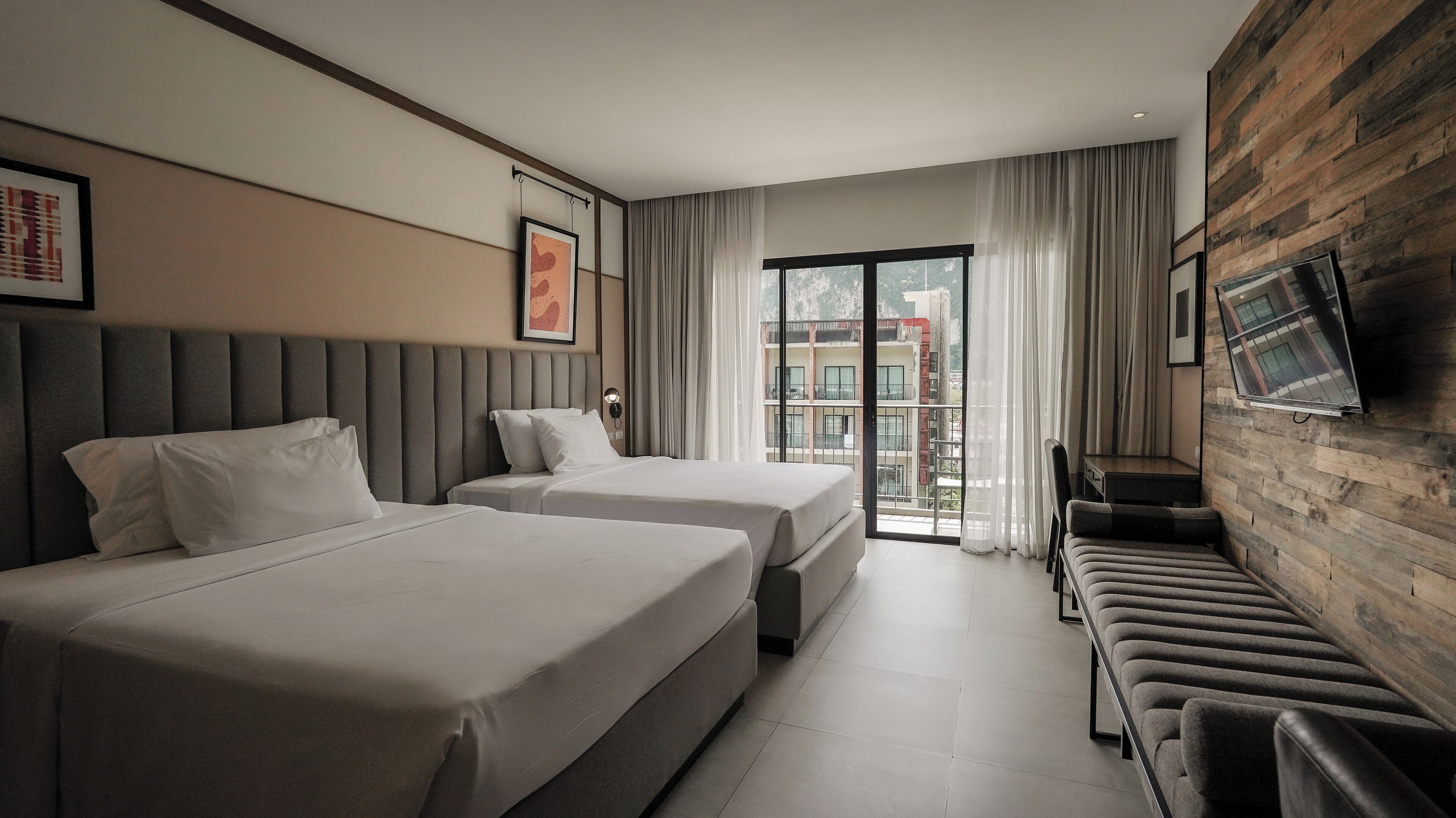 Habitación de hotel con dos camas, un sofá, un televisor y un balcón con vistas a edificios.