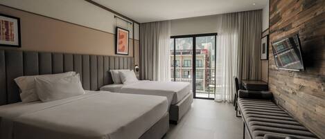 Habitación de hotel con dos camas, un sofá, un televisor y un balcón con vistas a edificios.