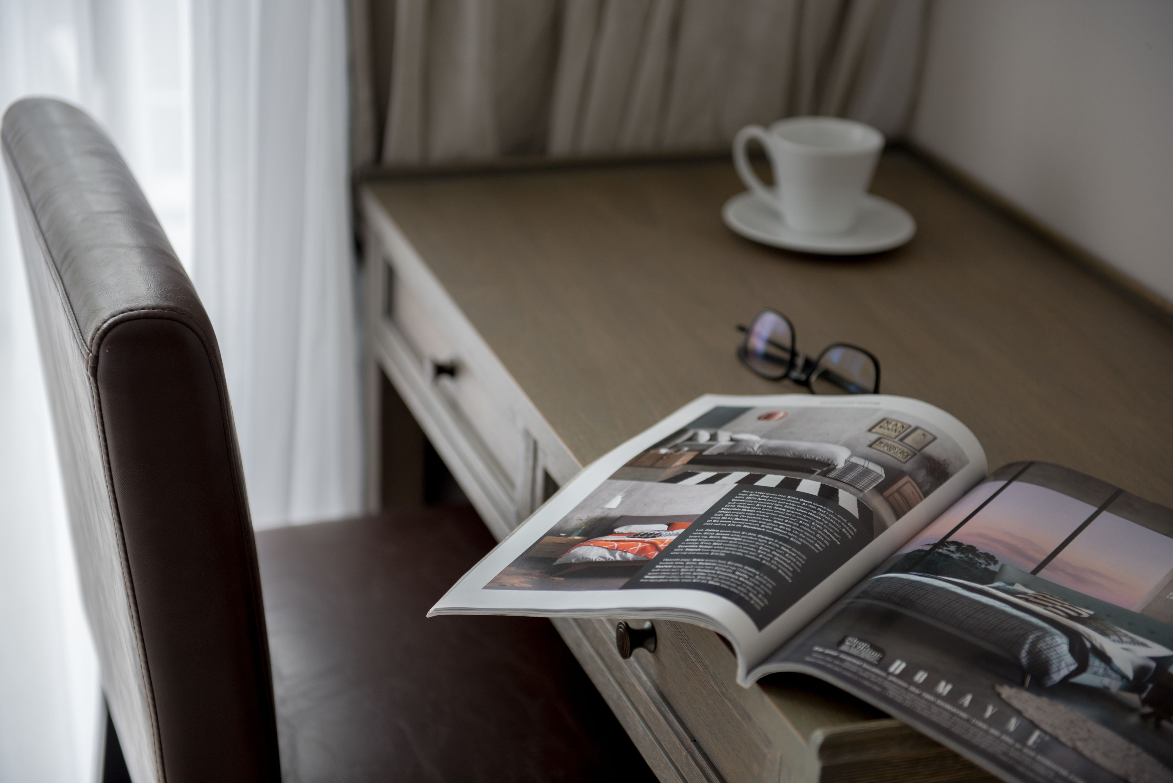 Una revista sobre una mesa, un par de lentes y una taza blanca.