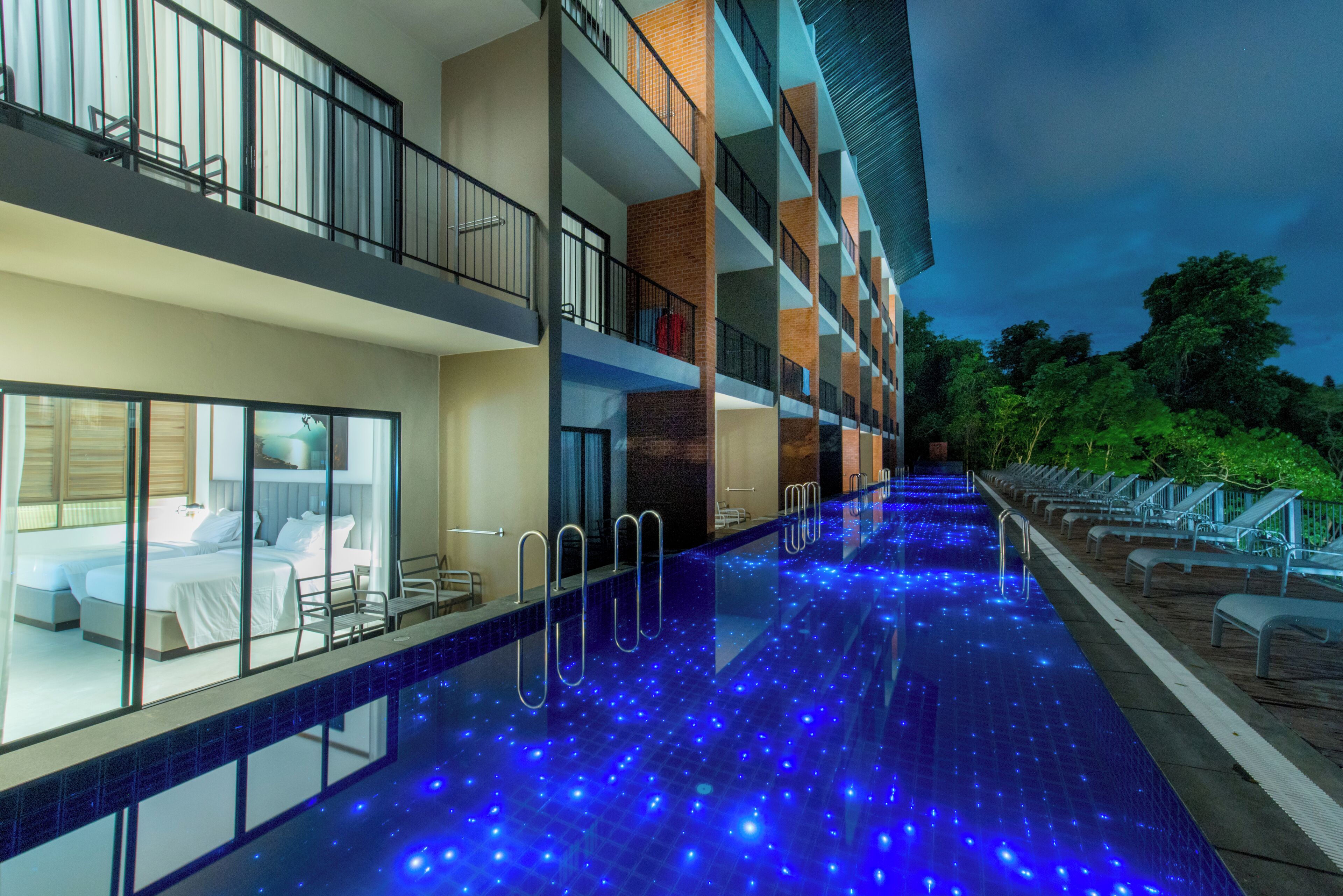 Hotel con piscina iluminada con luces LED azules, balcón con vista a la piscina y un interior bien iluminado.