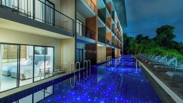 Hotel con piscina iluminada con luces LED azules, balcón con vista a la piscina y un interior bien iluminado.