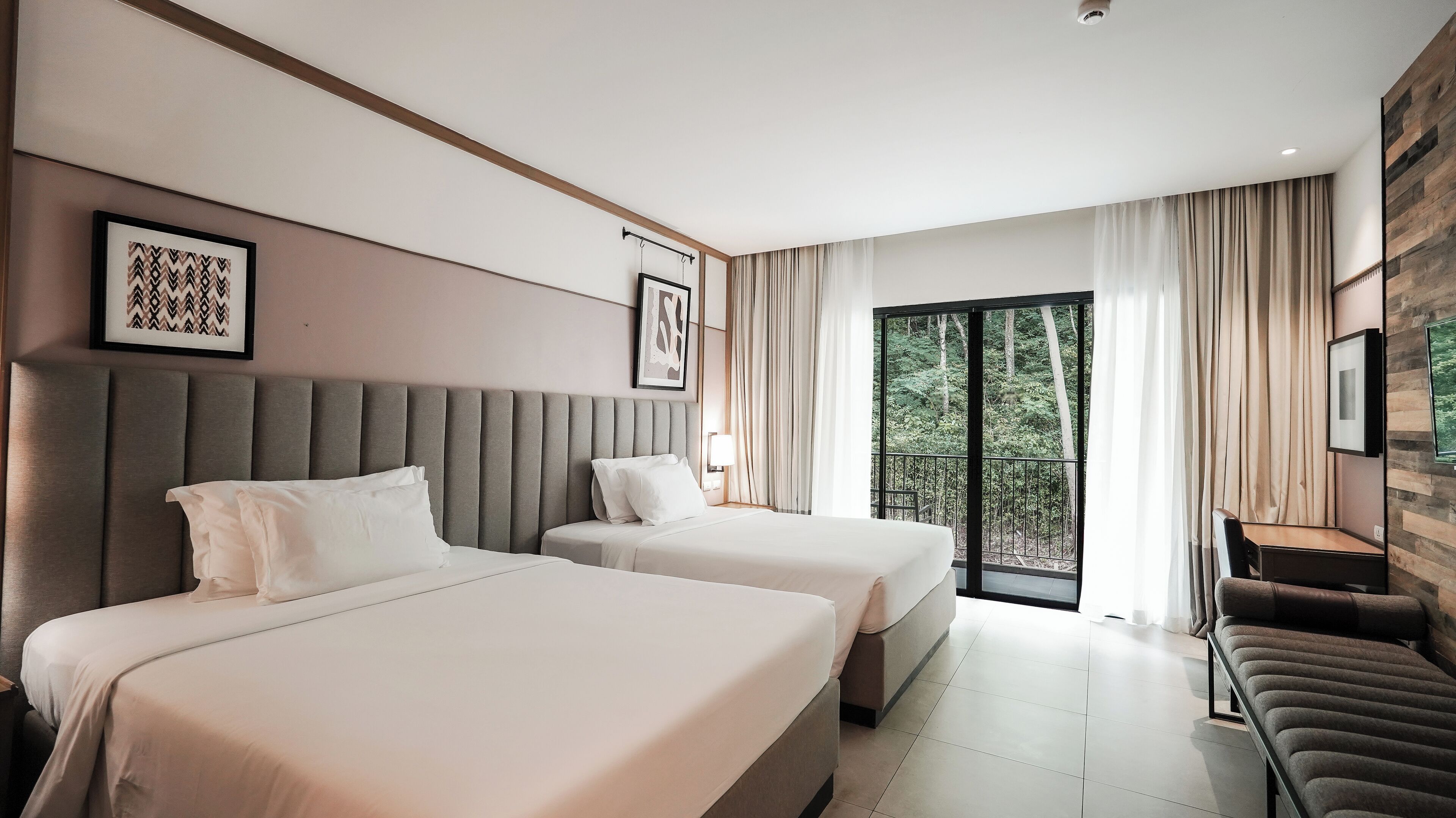 Ein modernes Hotelzimmer mit zwei Betten, einem Schreibtisch und Blick ins Freie.