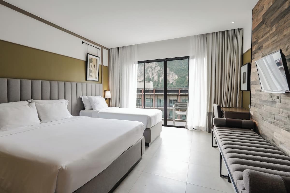 Habitación de hotel con dos camas, un sofá, un televisor y un balcón con vistas.