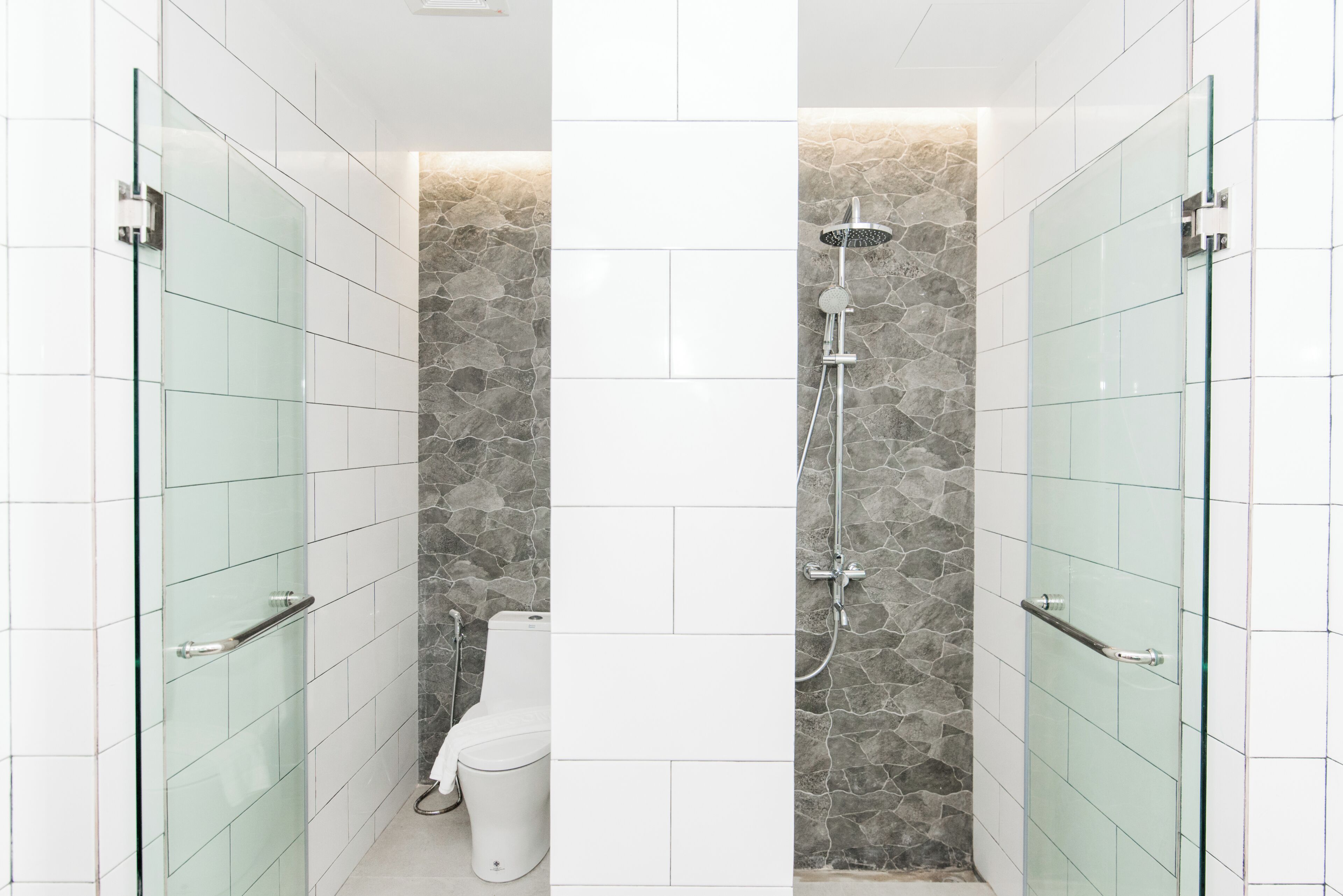 Une salle de bain moderne avec des portes de douche en verre, un mur d’accent en pierre et des toilettes blanches.
