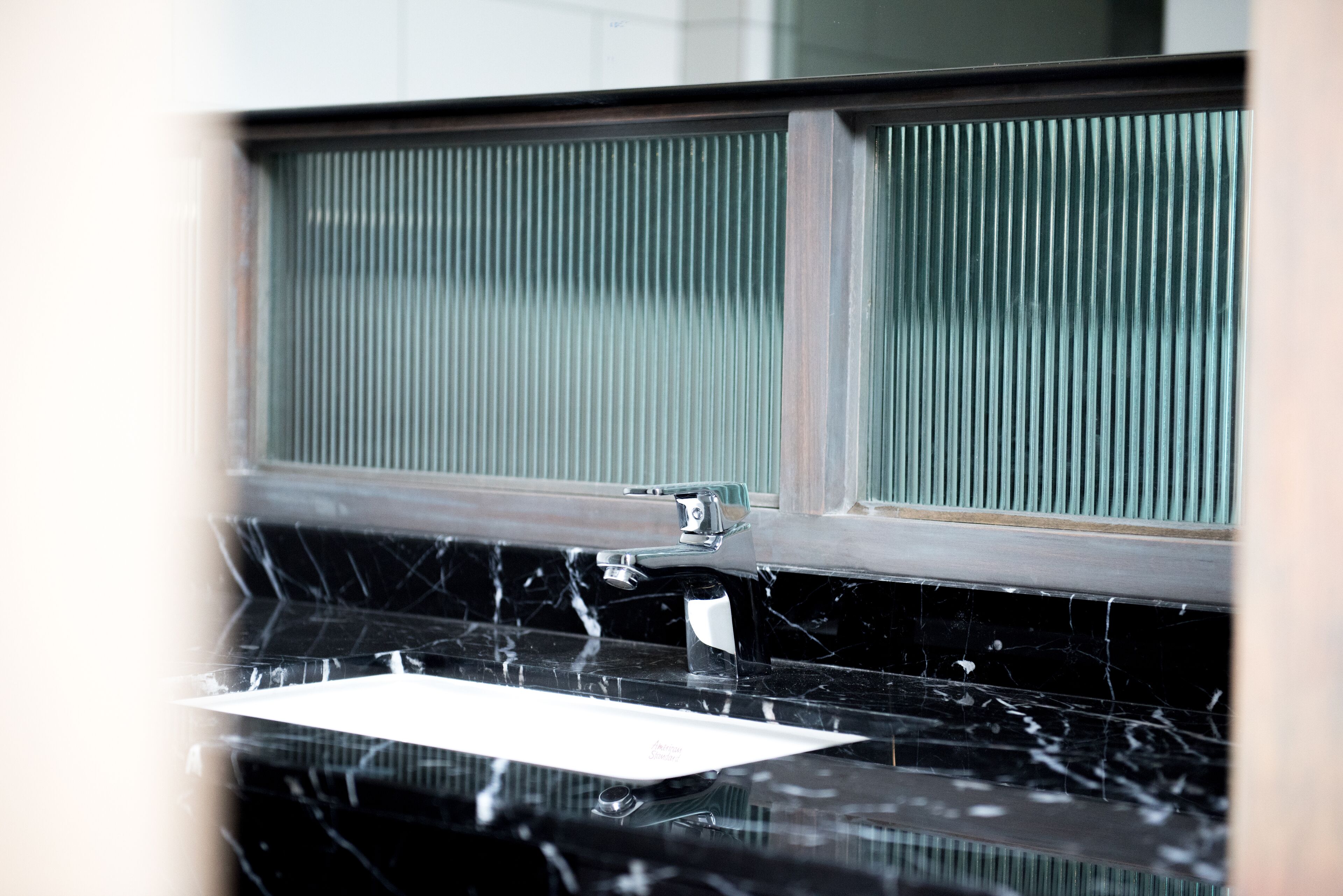 Un baño con lavamanos de mármol negro, un espejo y una ventana con persianas verticales.