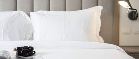 Uma cama bem arrumada com lençóis brancos, uma câmera sobre a cama e um abajur na mesa de cabeceira.