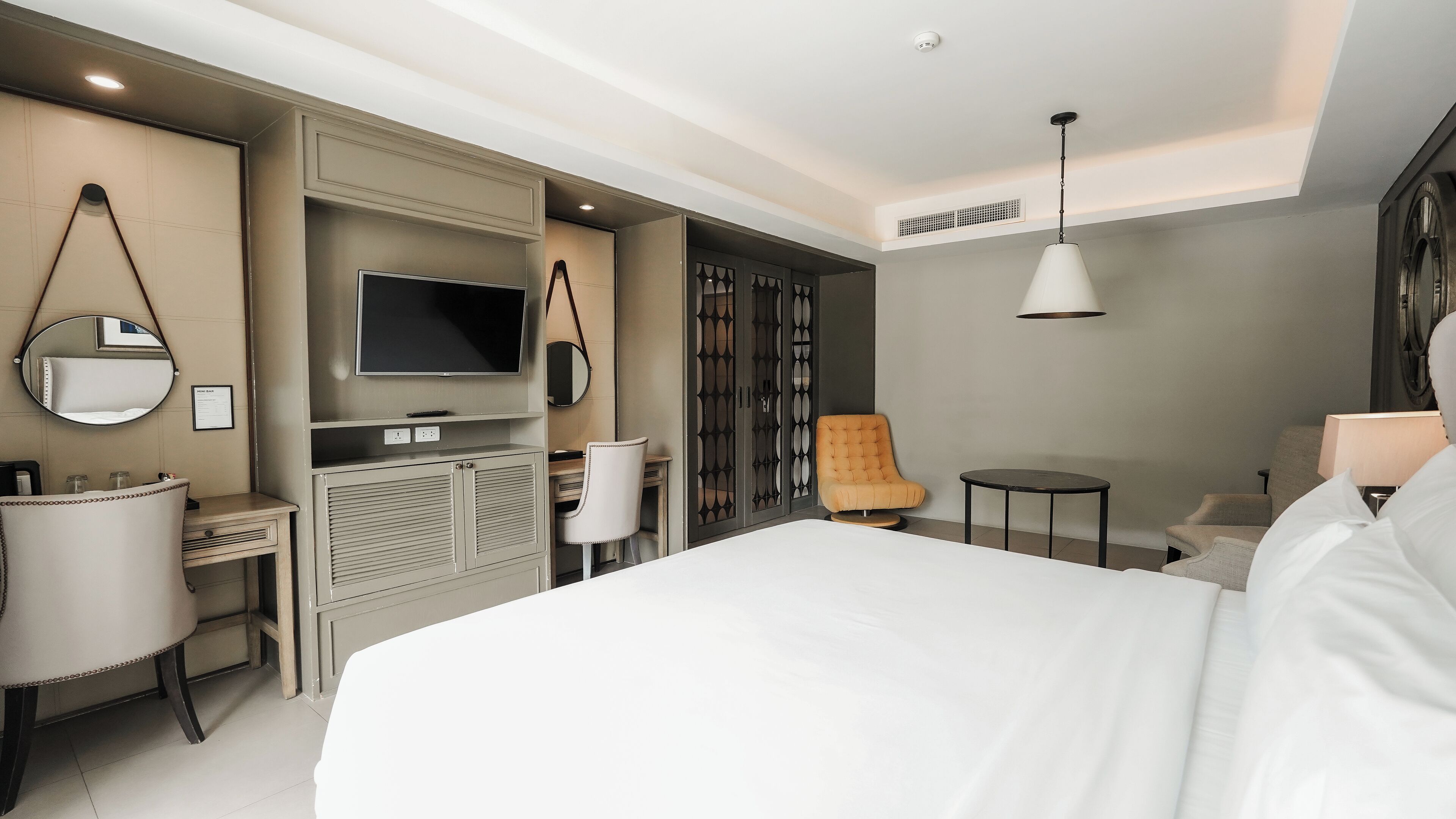 A modern hotel room with a large bed, a TV, a desk, a chair, and a small table.