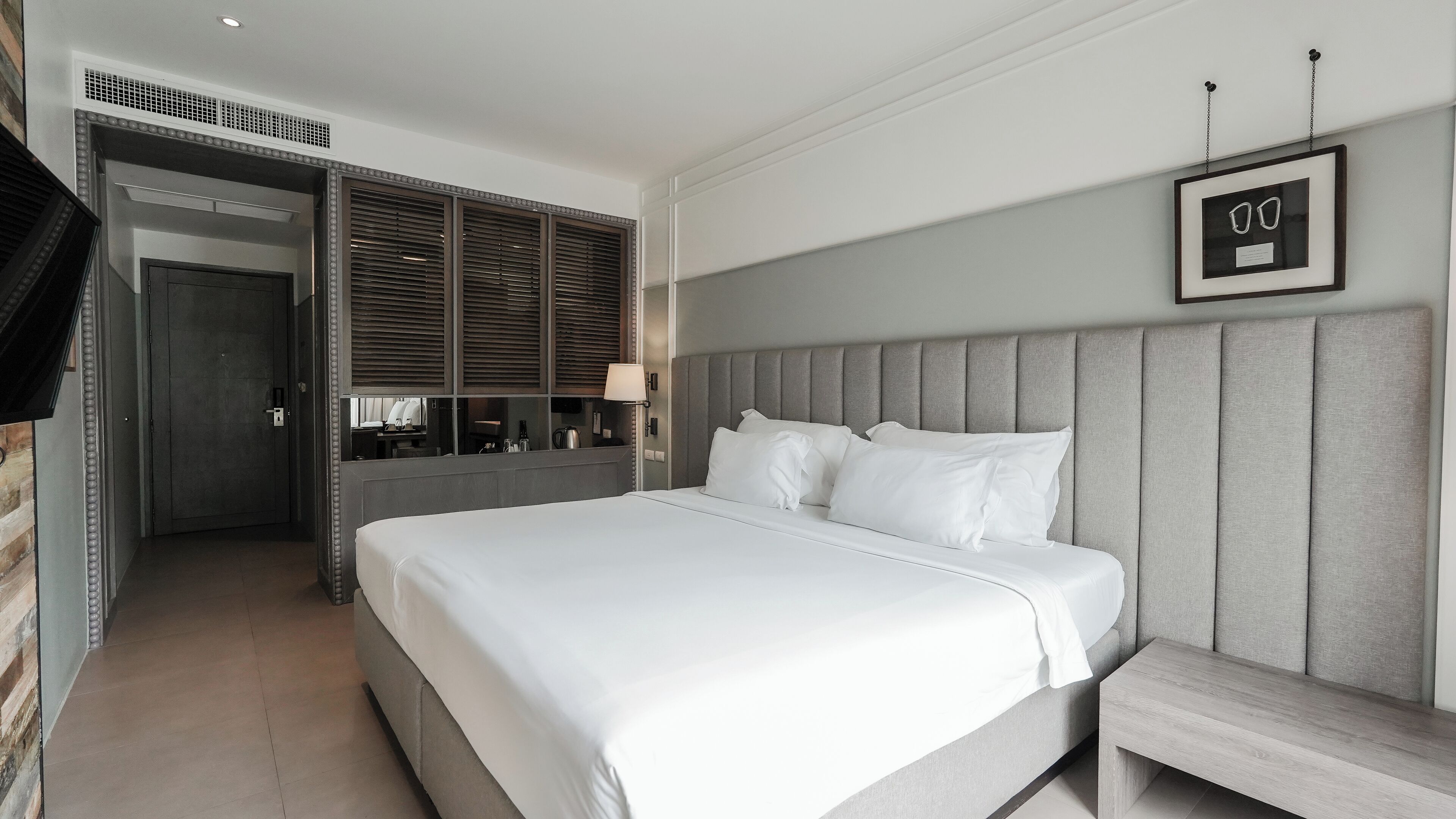 Una habitación de hotel moderna con una cama grande, una mesita de noche, un espejo y un cuadro en la pared.