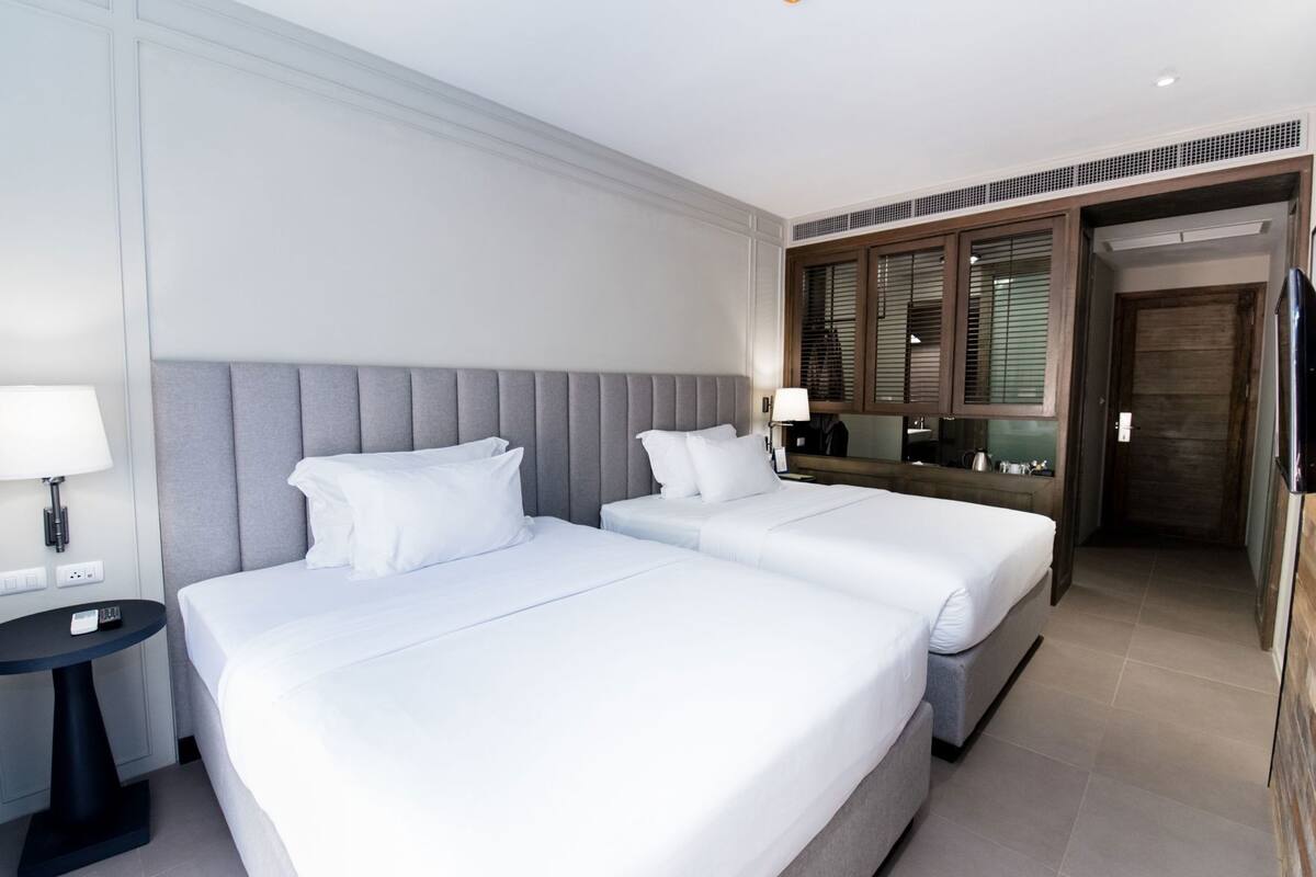 Una habitación de hotel con dos camas, una mesita de noche, una lámpara, un televisor y una puerta de madera.