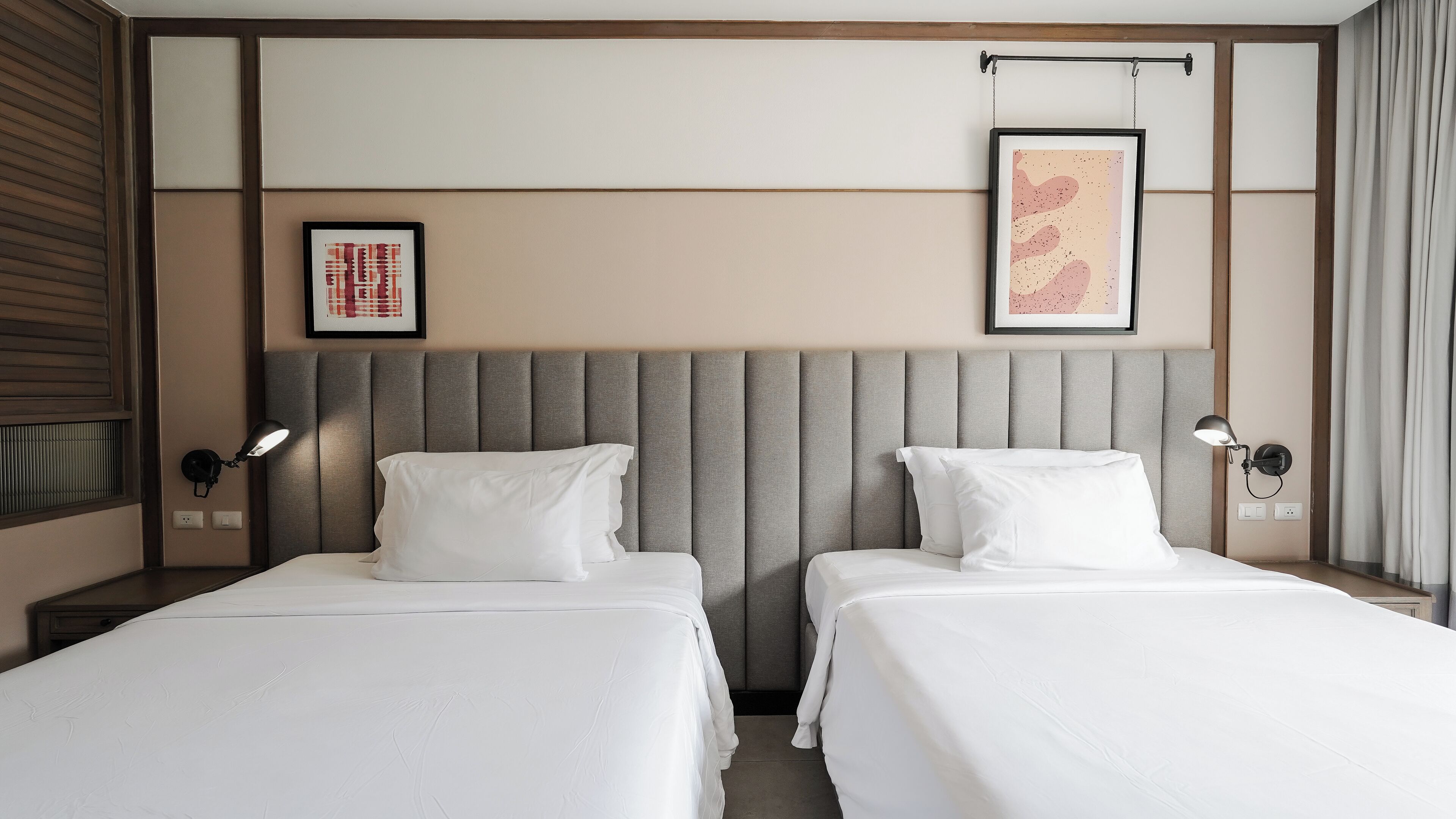 A hotel room with two beds, a padded headboard, wall-mounted lamps, and framed artwork.