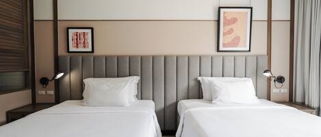 A hotel room with two beds, a padded headboard, wall-mounted lamps, and framed artwork.