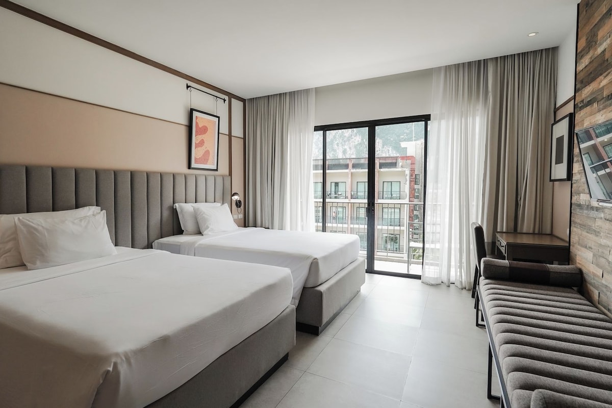 Une chambre d’hôtel avec deux lits, un canapé, un balcon avec vue et des œuvres d’art aux murs.