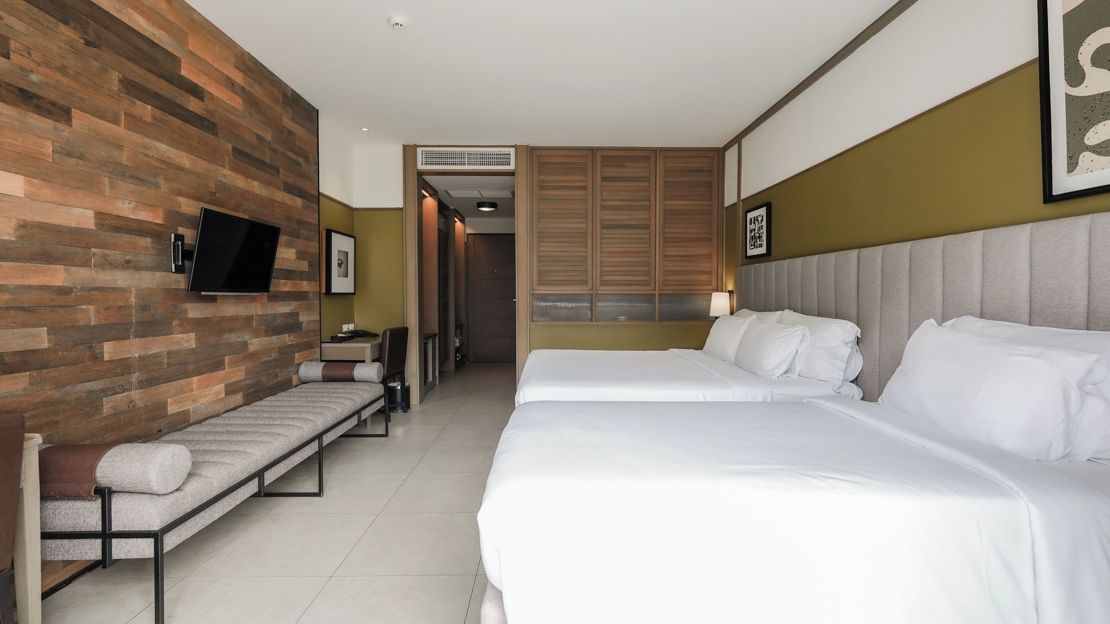 A hotel room with two beds, a sofa, a desk, and a TV mounted on the wall.