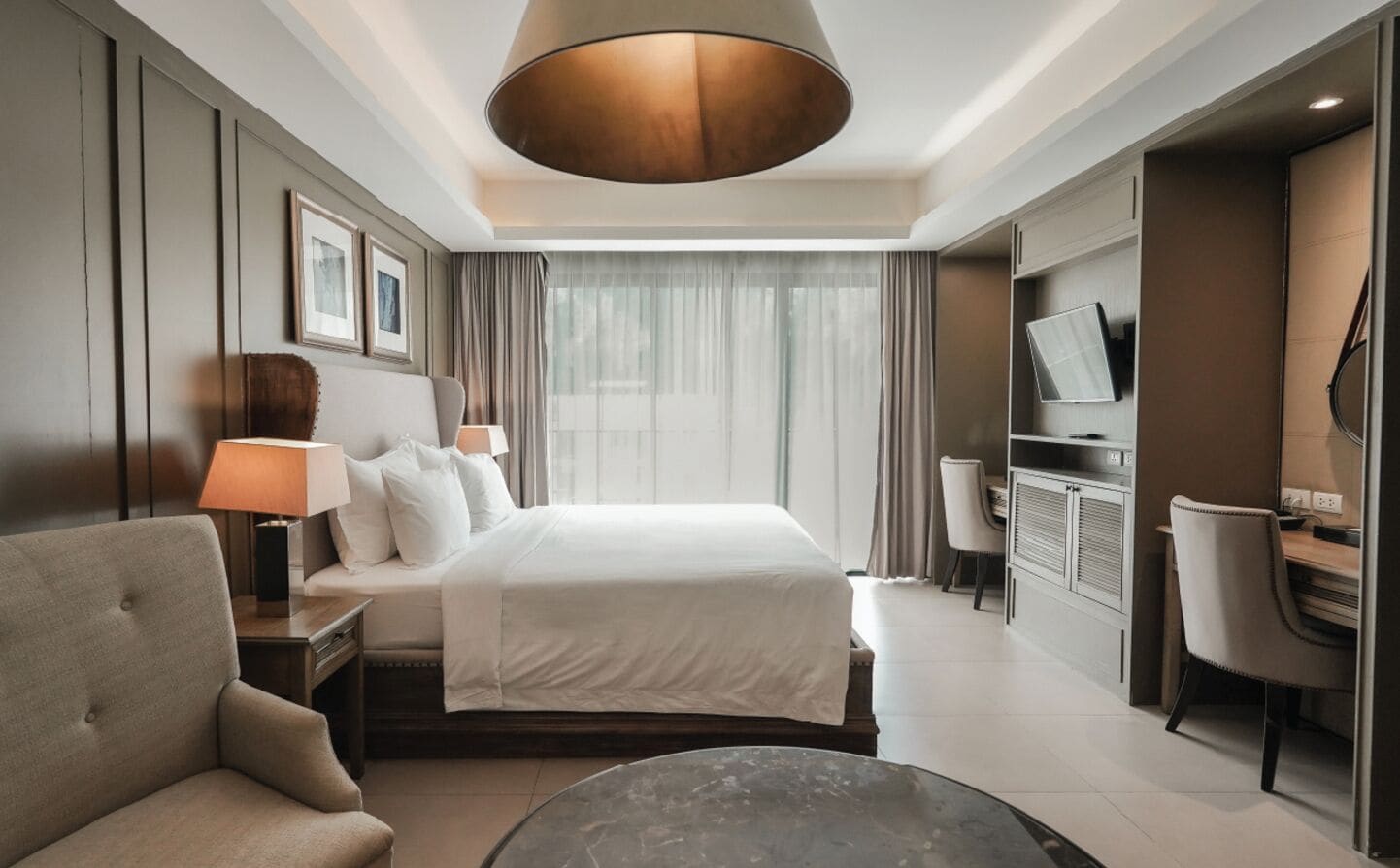 A hotel room with a bed, a desk, a chair, a TV, and a lamp.